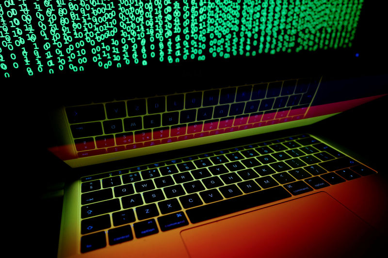 © Reuters. Fotocomposición de una bandera alemana reflejada en un portátil frente a una pantalla de computador con un código cibernético desplegado.