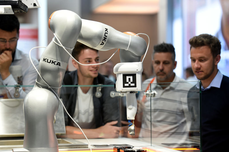 © Reuters. Visitors inspect a robot at the booth of KUKA at Hannover Messe, the trade fair in Hanover