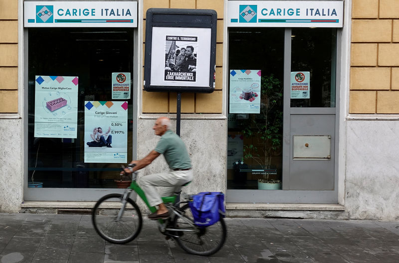 © Reuters. FILE PHOTO: A man rides a bicycle past a Carige bank in Rome