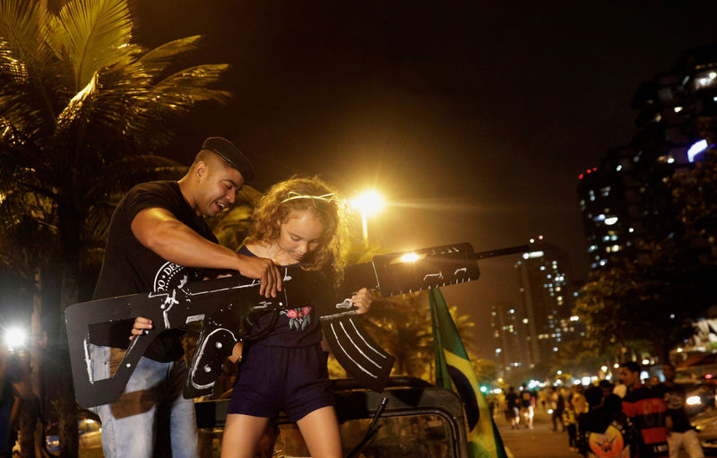 © Reuters. Apoiador de Bolsonaro ajuda menina a segurar arma de papelão, no Rio de Janeiro