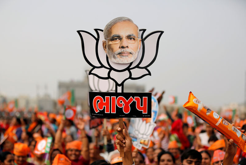 © Reuters. FILE PHOTO: A supporter holds up a cut-out of lotus, the election symbol of India's ruling BJP, with an image of PM Modi during a campaign meeting addressed by Modi ahead of Gujarat state assembly election in Kalol