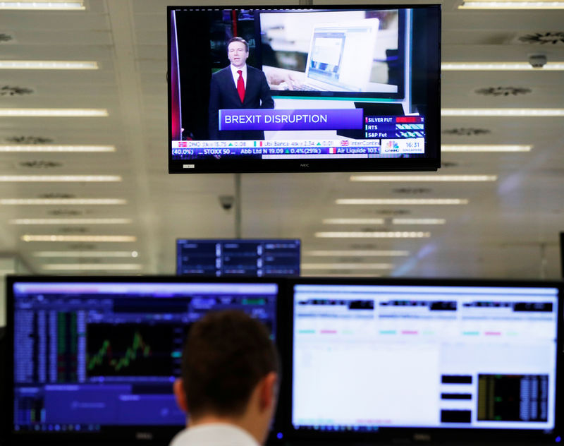 © Reuters. Trader watches a television screen as he works at his desk whilst screens show market data at CMC Markets in London