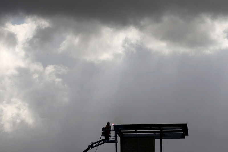 © Reuters. FILE PHOTO:  A construction worker welds under stormy clouds high atop a structure being built by the U.S. Government next to the Mexican border in San Diego