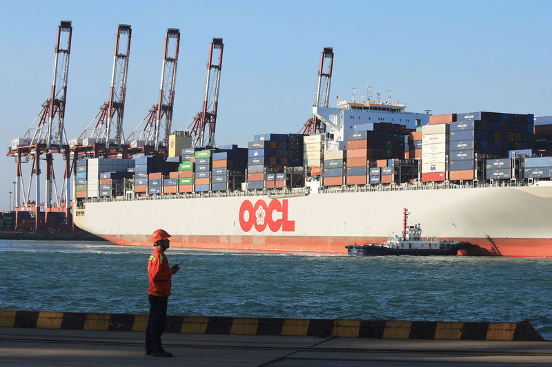 © Reuters. Worker stands in front of an OOCL container ship at a port in Qingdao