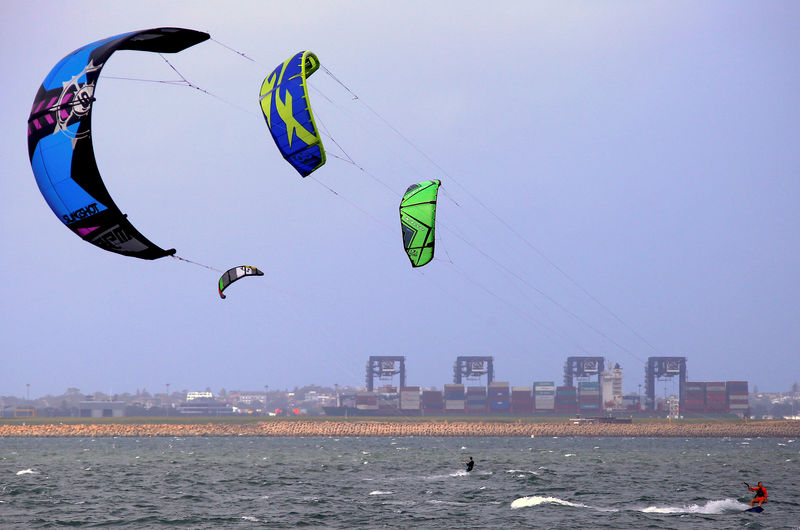 © Reuters. Kite surfers can be seen in front of a container ship docked at the Port Botany Container terminal on a windy day in Sydney