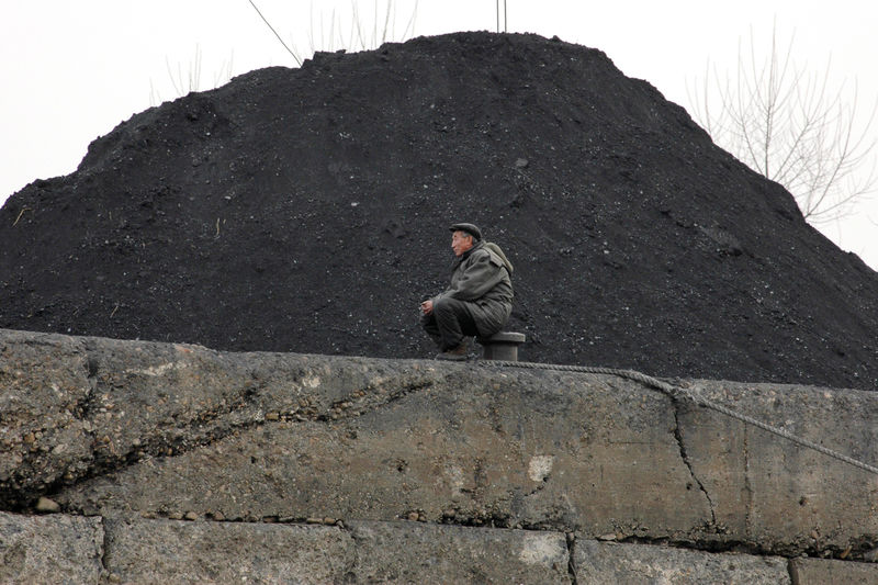 © Reuters. FOTO DE ARCHIVO: un hombre norcoreano sentado junto a una pila de carbón en la orilla del río Yalu en la ciudad norcoreana de Sinuiju
