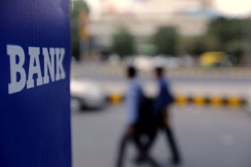 © Reuters. FILE PHOTO: Commuters walk past a bank sign along a road in New Delhi