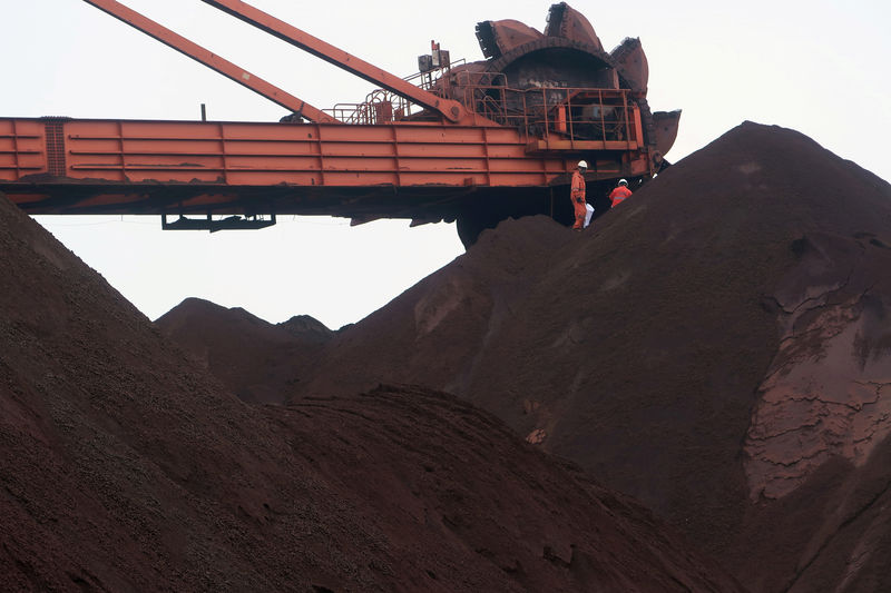 © Reuters. FILE PHOTO: Workers are seen on the top of an iron ore pile as a machine works on blending the iron ore, at Dalian Port