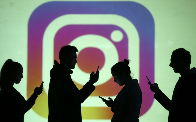 © Reuters. FILE PHOTO - Silhouettes of mobile users are seen next to a screen projection of Instagram logo in this picture illustration