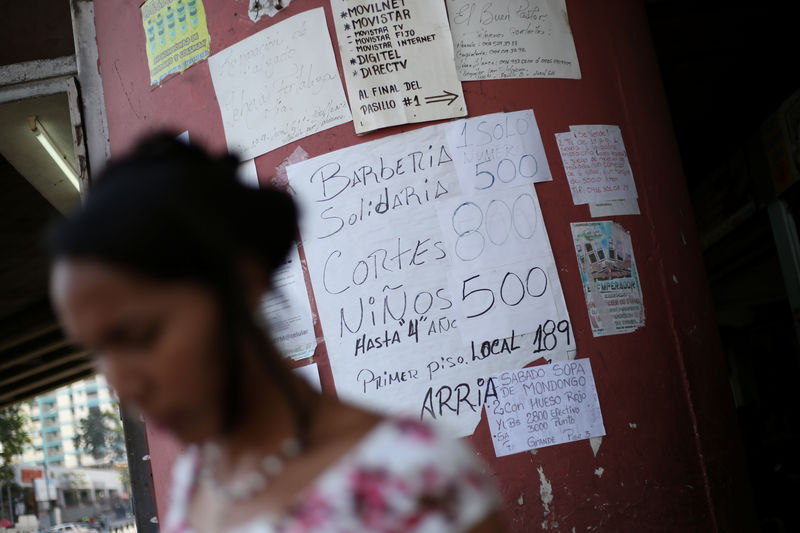 © Reuters. A woman walks past placards with prices of different products and services in a street of Caracas