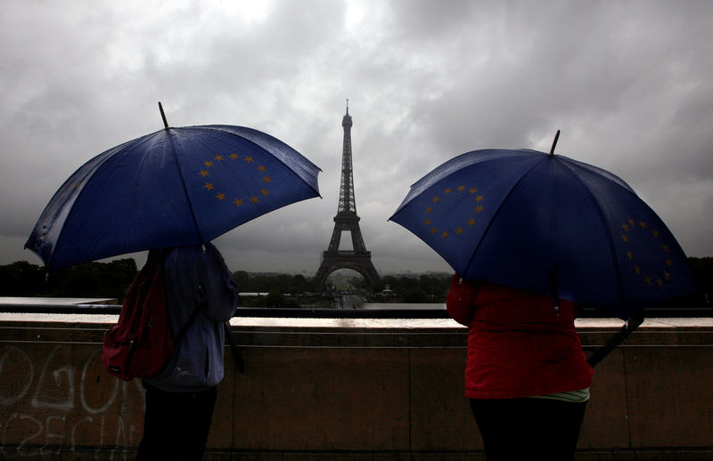 © Reuters. Tourists protect themselves from the rain under umbrellas in front of the Eiffel tower as they visit the French capital during summer holidays in Paris