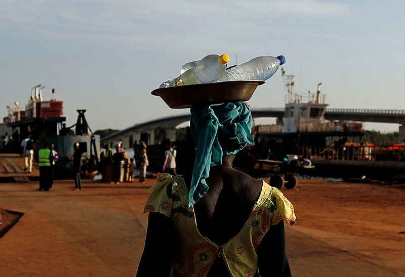 © Reuters. A woman street vendor waits for customers at the ferry's terminal beside the newly inaugurated Sene-Gambia bridge, that links  South to the North Gambia's banks  in Farafenni-Soma