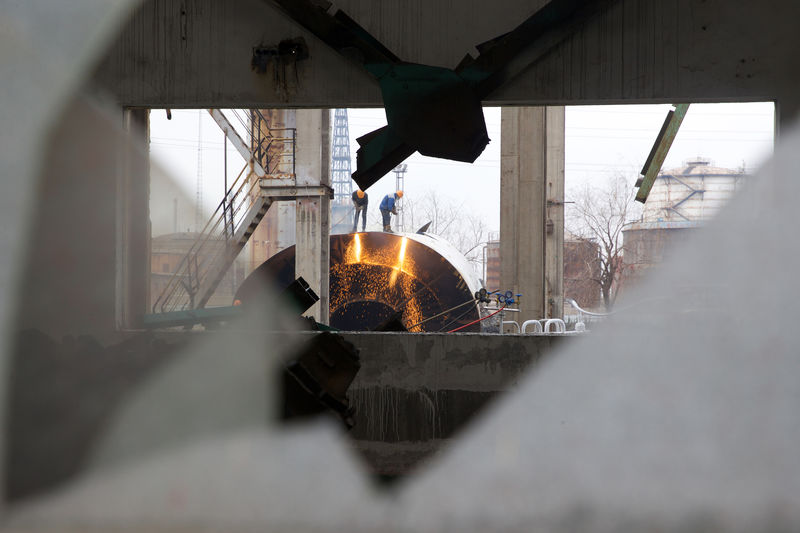 © Reuters. Labourers working on dismantling equipment and facilities are seen through a window at a former steel factory of Jigang, in Jinan