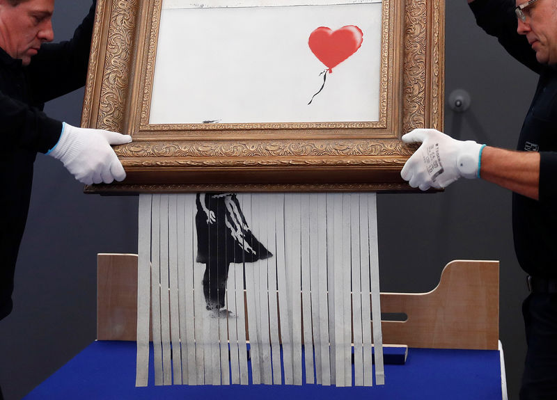© Reuters. Empleados del Frieder Burda Museum sostienen la obra de arte parcialmente destrozada de Banksy "El amor está en la papelera"
