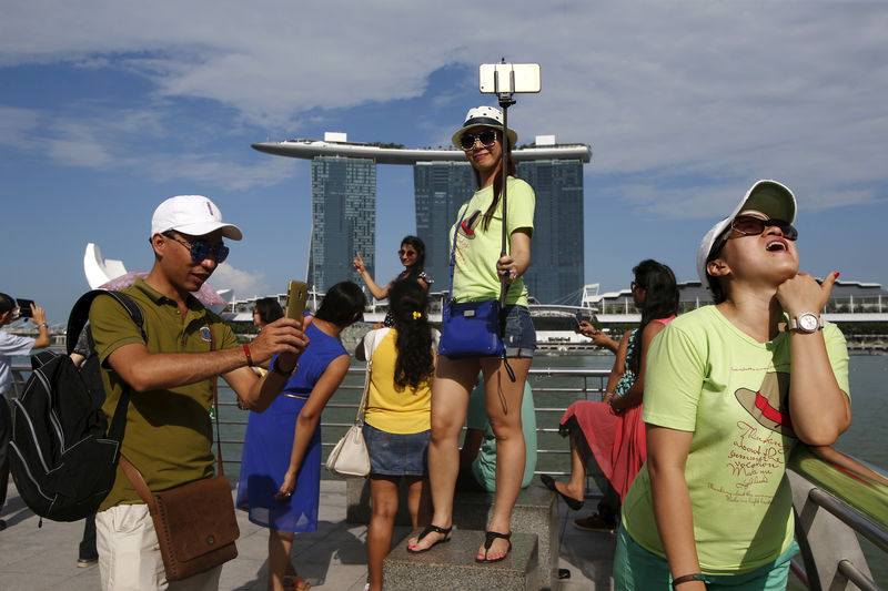 © Reuters. FILE PHOTO - Tourists pose for photos with the Marina Bay Sands and the Merlion statue at a popular tourist spot along Marina Bay in Singapore