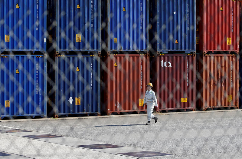 © Reuters. FILE PHOTO: Worker walks between shipping containers at a port in Tokyo