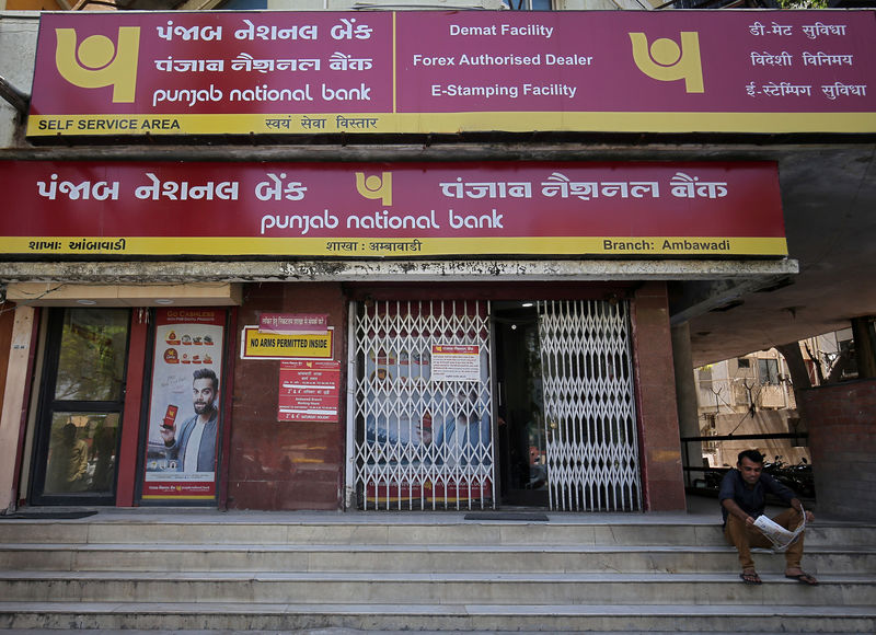 © Reuters. FILE PHOTO:  A man reads a newspaper outside a branch of Punjab National Bank in Ahmedabad