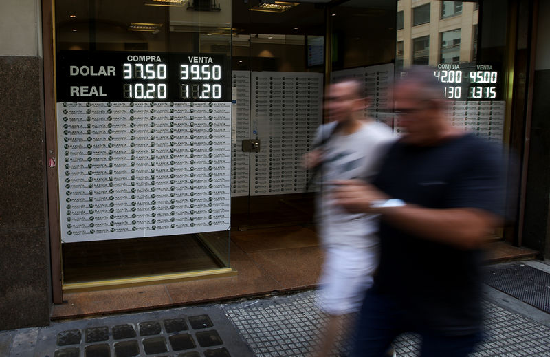 © Reuters. Pedestrians walk past an electronic board showing currency exchange rates in Buenos Aires' financial district