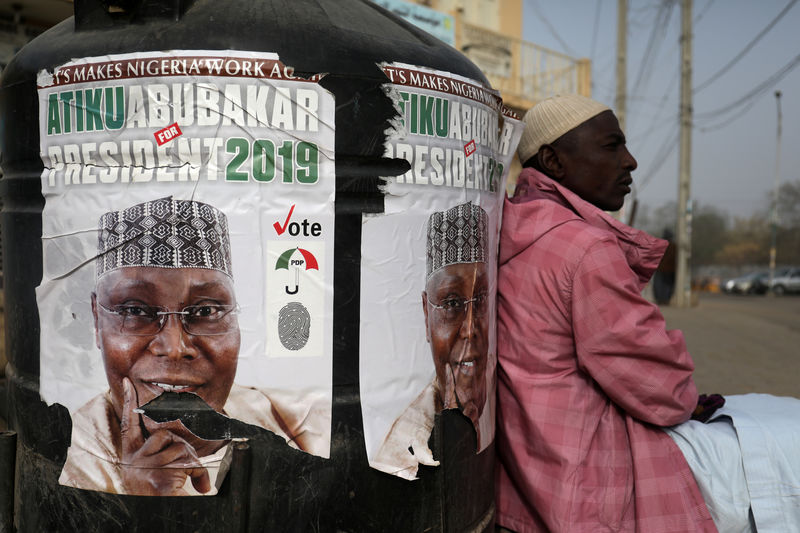 © Reuters. FILE PHOTO: A man sits next to a campaign poster of Atiku Abubakar, leader of the People's Democratic Party (PDP), after the postponement of the presidential election in Kano