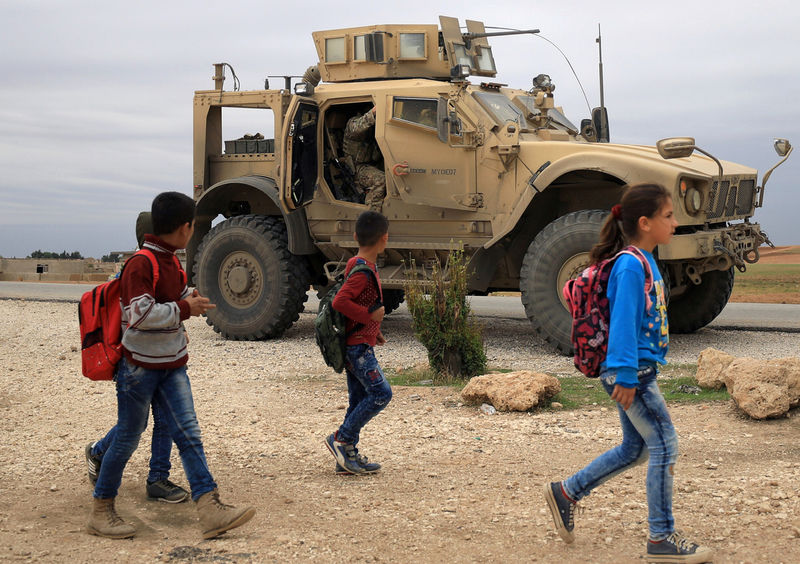 © Reuters. FILE PHOTO: Syrian schoolchildren walk as U.S. troops patrol near Turkish border in Hasakah
