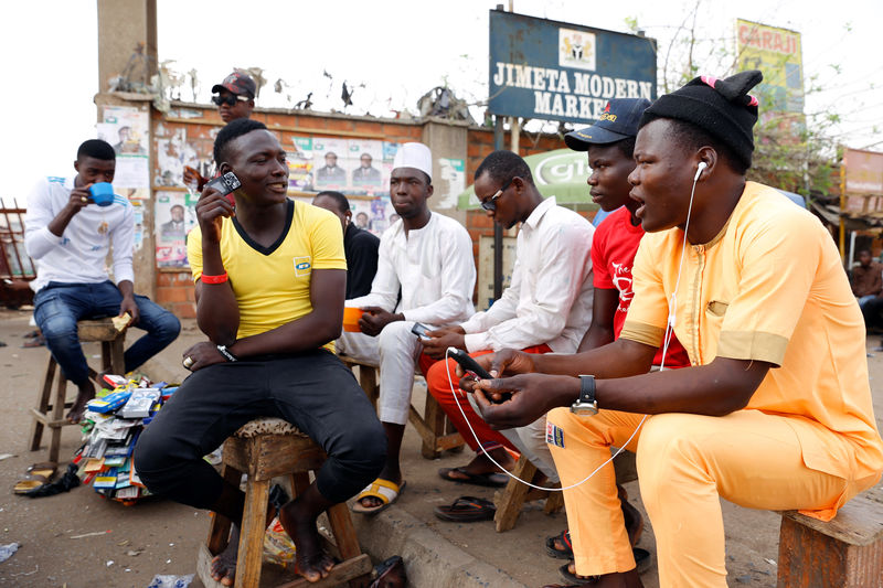 © Reuters. Youths listen to news on their mobile phones as Nigerians await the results of the Presidential election, in Yola