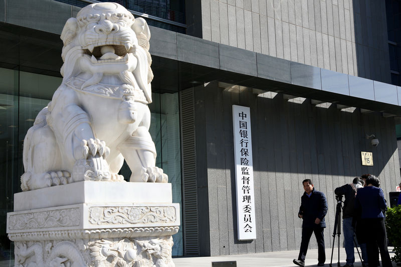 © Reuters. FILE PHOTO:  People film the new sign of CBIRC, the newly merged regulatory body, at its office in Beijing