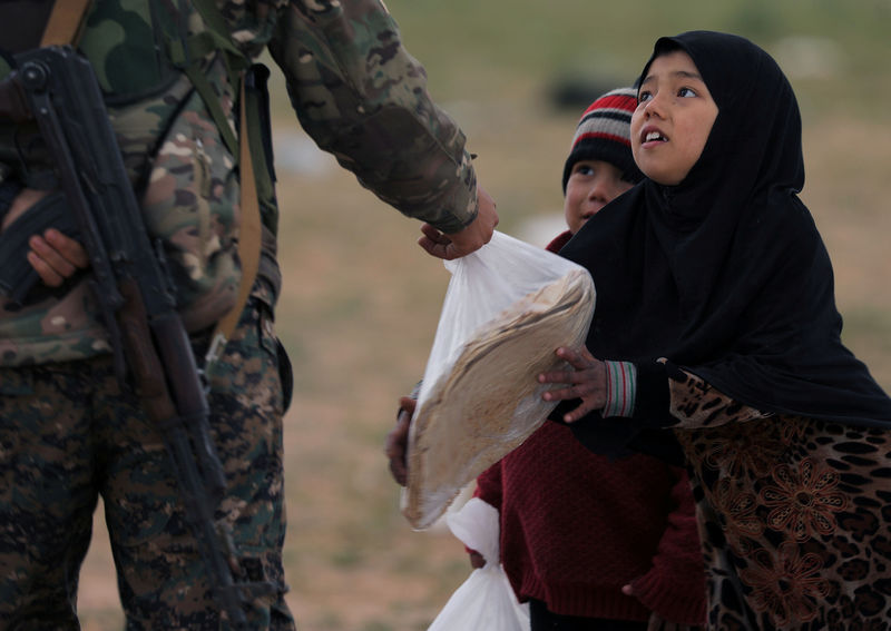 © Reuters. Garota pega um pedaço de pão das mãos de um combatente das Forças Democráticas da Síria perto da vila de Baghouz