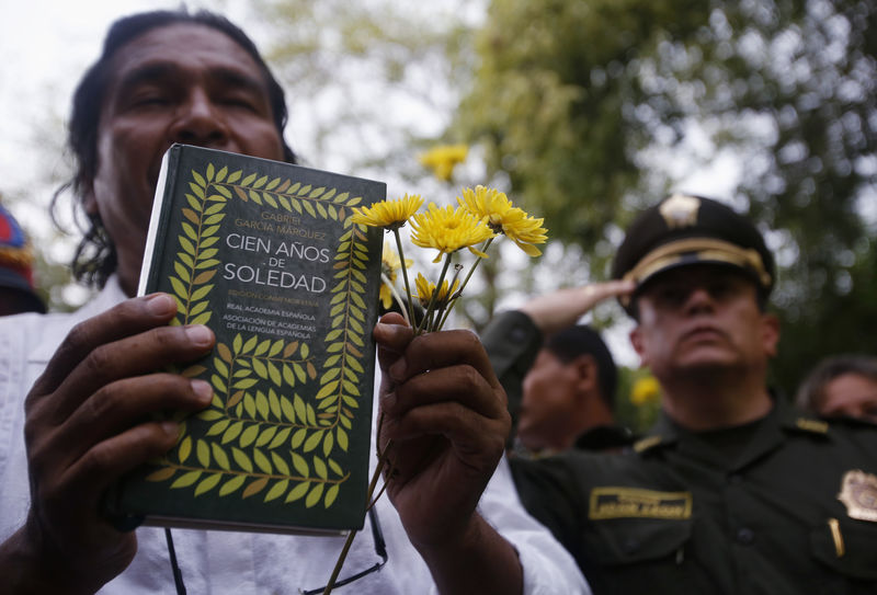 © Reuters. Una persona que sostiene flores y un libro "Cien años de soledad" del premio Nobel colombiano Gabriel García Márquez participa en un funeral simbólico del escritor en Aracataca, Colombia.