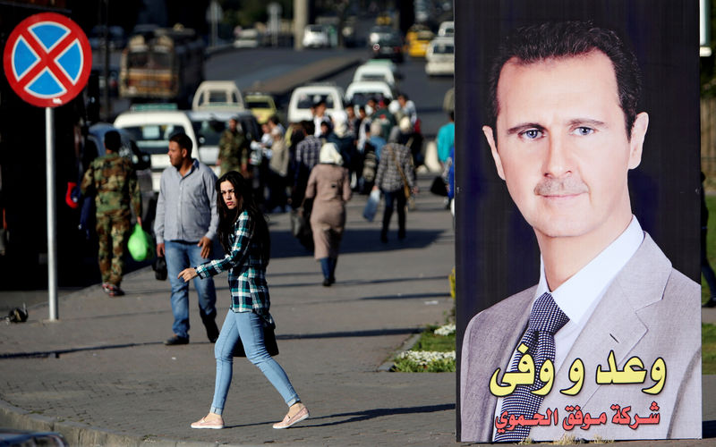 © Reuters. FILE PHOTO: A woman walks near a picture of Syrian President Bashar al Assad in Damascus.