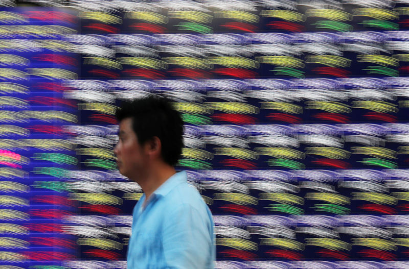 © Reuters. FILE PHOTO: Passersby walk past in front of an electronic stock quotation board outside a brokerage in Tokyo