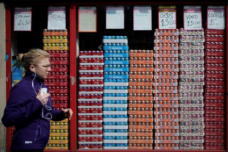 © Reuters. A woman walks past a shop window with cans of soda in Paris