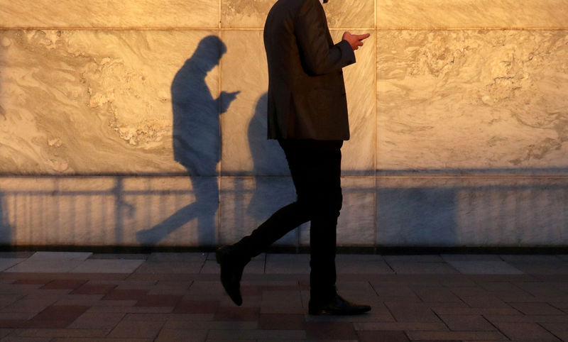 © Reuters. FILE PHOTO: An unidentified man using a smart phone walks through London's Canary Wharf financial district in the evening light in London