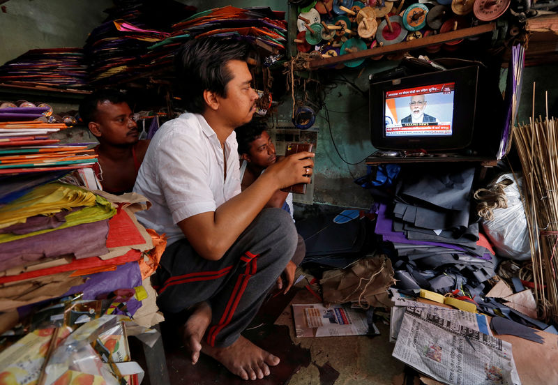 © Reuters. Men watch Prime Minister Narendra Modi addressing to the nation, on a TV screen inside their shop in Kolkata