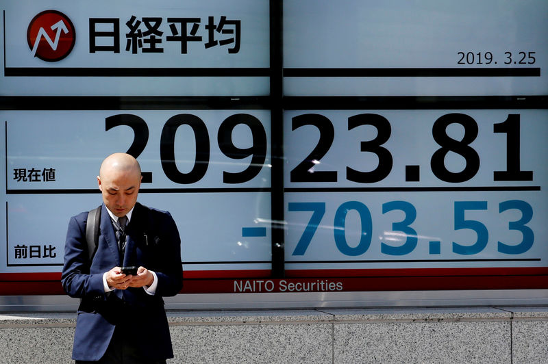 © Reuters. FILE PHOTO: A man stands in front of an electronic board showing the Nikkei stock index outside a brokerage in Tokyo