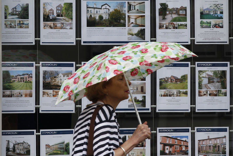 © Reuters. FILE PHOTO: A woman holds an umbrella as she walks past the window of an estate agents office in Manchester