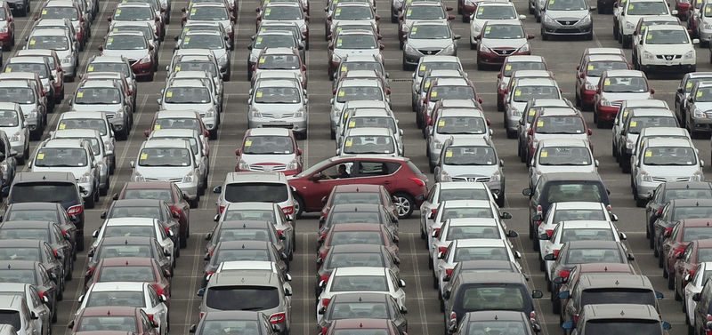 © Reuters. FILE PHOTO: Man drives red car past parking lot where large numbers of newly manufactured cars are parked at Dayaowan port of Dalian