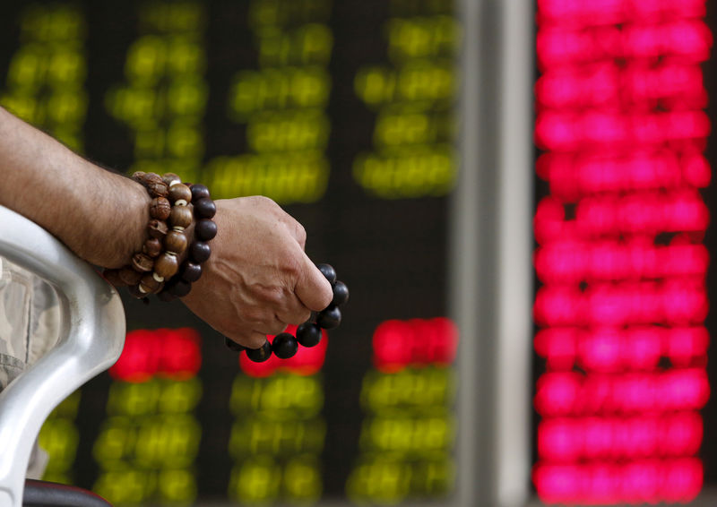 © Reuters. An investor holds onto prayer beads as he watches a board showing stock prices at a brokerage office in Beijing