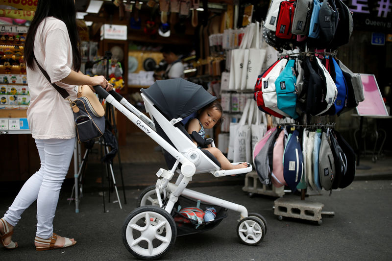 © Reuters. FILE PHOTO: A woman pushing her baby in a stroller shops in the Hongdae area of Seoul