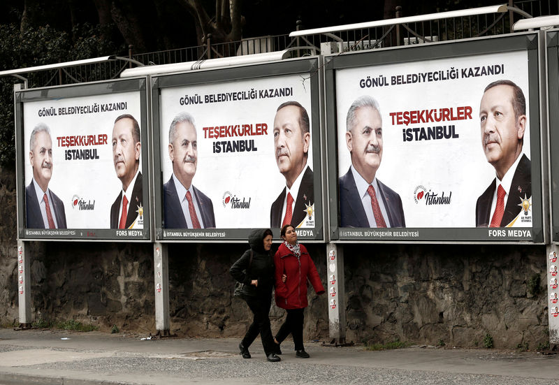 © Reuters. FILE PHOTO: People walk past by AK Party billboards with pictures of Turkish President Tayyip Erdogan and mayoral candidate Binali Yildirim in Istanbul