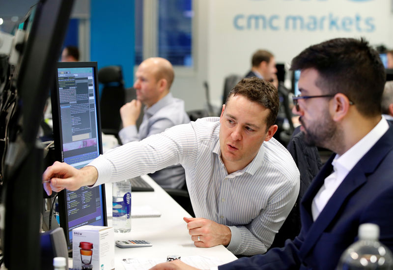 © Reuters. Traders work at their desks at CMC Markets in London