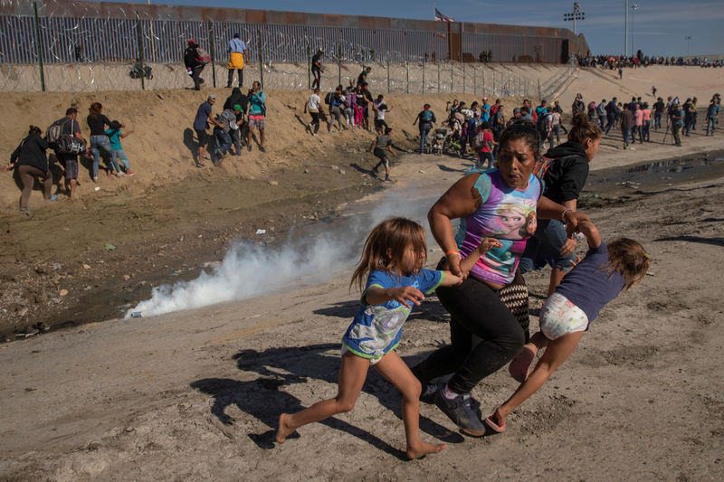 © Reuters. Maria Meza runs away from tear gas with her five-year-old twin daughters Saira Mejia Meza and Cheili Mejia Meza in front of the border wall