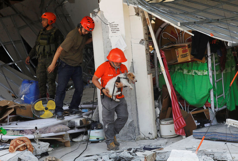 © Reuters. Socorrista carrega cão usado nas buscas em prédio que desabou após terremoto nas Filipinas