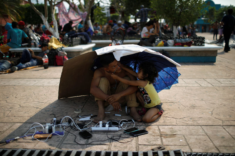 © Reuters. A migrant from Honduras watch other migrants' cellphones as they gather in an improvised shelter during a break in their journey towards the United States, in Escuintla