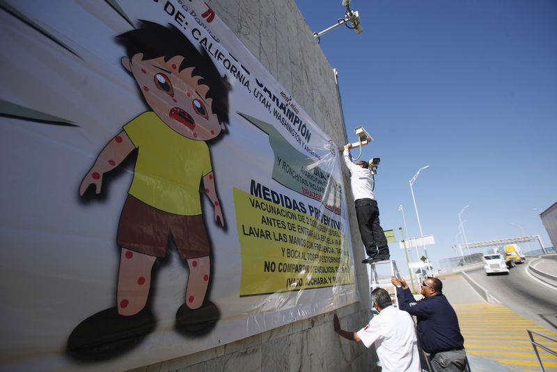 © Reuters. Imagen de archivo de un trabajador colocando un letrero sobre el programa de prevención del sarampión durante una campaña de concienciación de trabajadores de la salud en el cruce fronterizo de Ciudad Juárez en México con El Paso, Texas