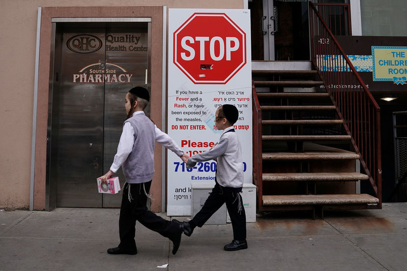 © Reuters. Dos niños judíos pasan frente a un cartel de advertencia sobre el brote de sarampión en el distrito de Brooklyn, Nueva York, EEUU.