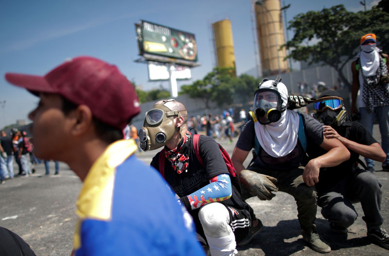 © Reuters. Manifestantes de la oposición se agachan y se cubren en una calle cerca de la base aérea del Generalísimo Francisco de Miranda "La Carlota" en Caracas