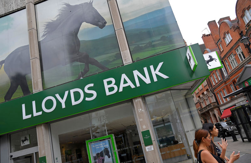 © Reuters. FILE PHOTO: A woman looks at her phone as she walks past a branch of Lloyds bank in London, Britain