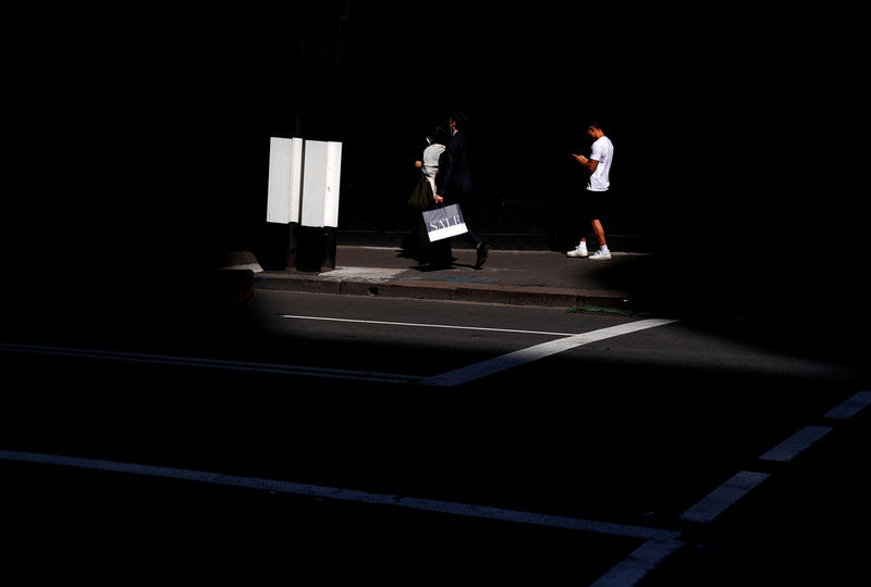 © Reuters. A man carries a bag displaying the word 'Sale' as he walks along a footpath with other pedestrians outside a retail store in central Sydney