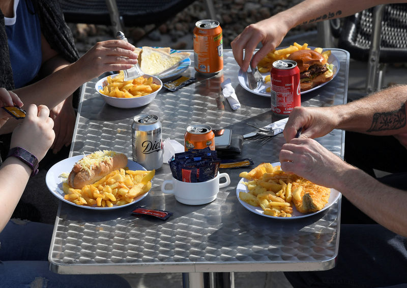 © Reuters. FILE PHOTO: Visitors eat fish and chips and drink soft drinks at a beach cafe in Brighton