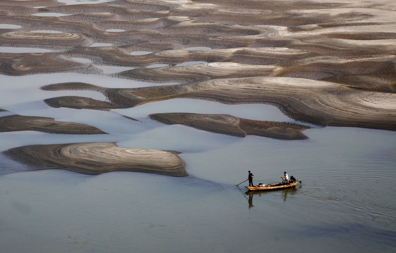 © Reuters. Two men row a boat past a partially dried-up riverbed on a section of the Yangtze River in Jiujiang